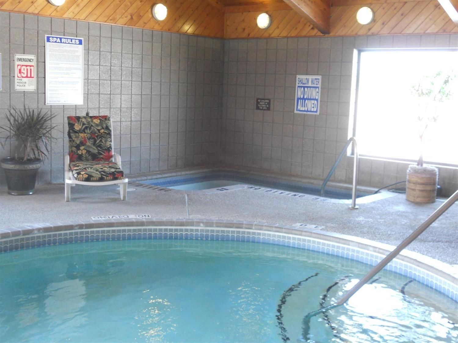 A pool area with a chair, a sign indicating shallow water, and emergency contact information on the wall.
