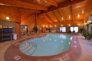 An indoor swimming pool with a wooden ceiling, lounge chairs, and a 'NO DIVING' sign.
