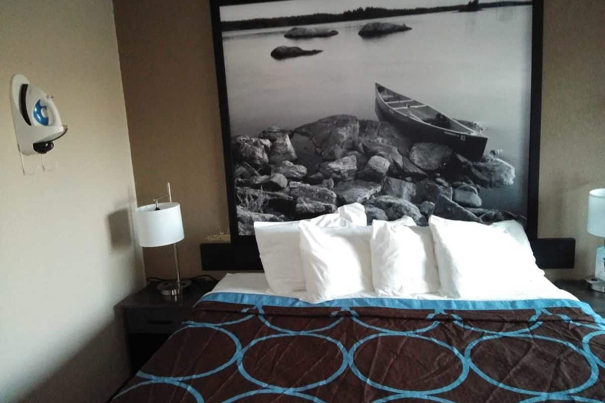 A hotel room with a bed, a nightstand, a lamp, and a large framed picture of a rocky landscape with a boat.
