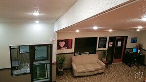 A reception area with a beige sofa, a reception desk, a wall-mounted sign detailing pool and spa area use, and a small potted plant.