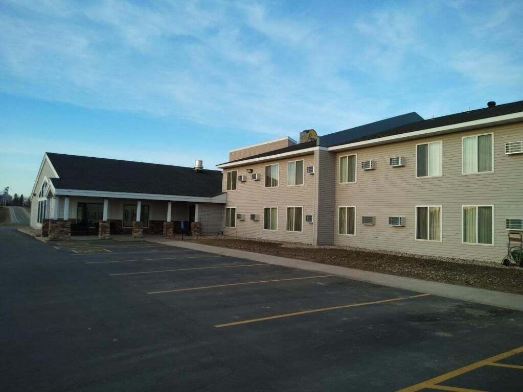 A hotel with a parking lot, a covered outdoor area, and a building with multiple windows and air conditioning units.