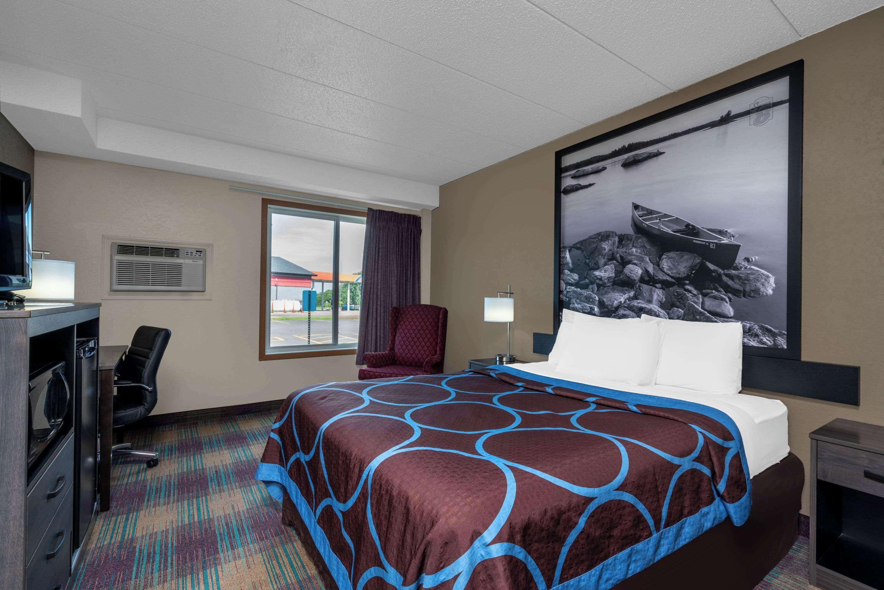 A hotel room with a large bed, a desk with a computer, a chair, a TV, and a window with a view of the outside.