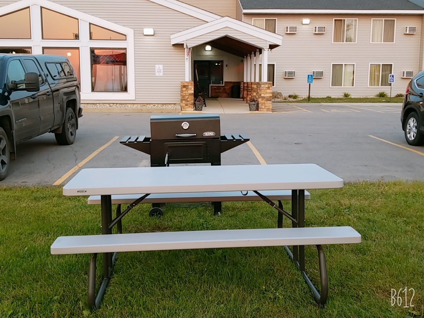 A picnic table in front of a building with a covered entrance and a parking lot.