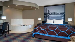 A hotel room with a large bed, a desk, a chair, a bathtub, and a cityscape view.