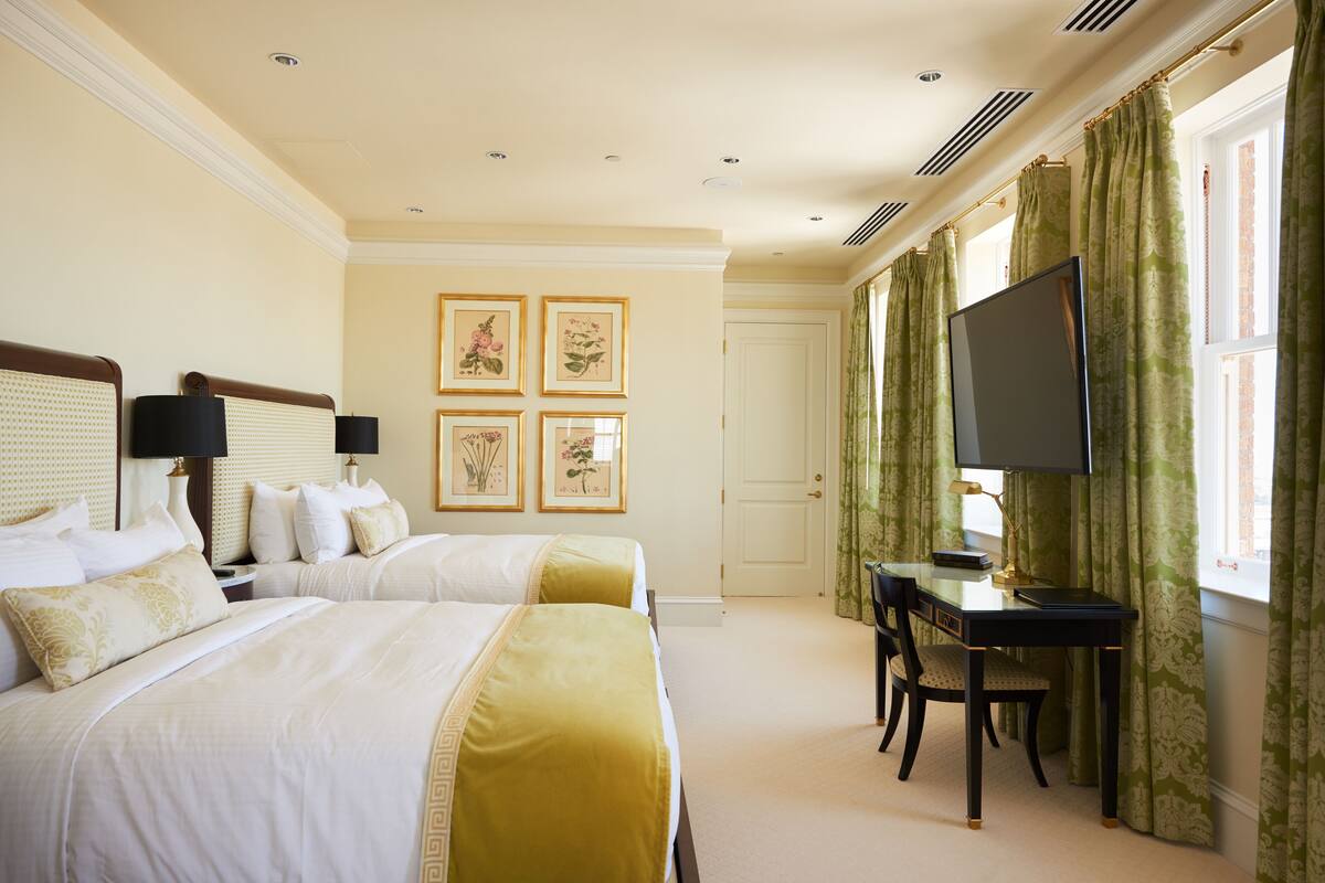 A hotel room with two beds, a desk with a chair, a television, and framed pictures on the wall.