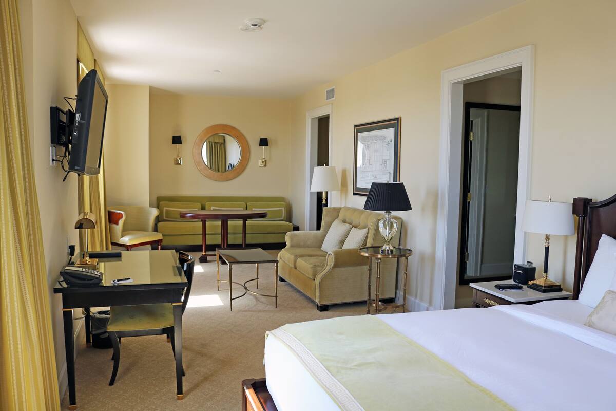 A hotel room with a bed, a desk, a chair, a sofa, a small table, and a lamp.
