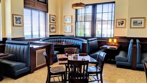 A restaurant with booth seating, framed pictures on the walls, and large windows with blinds. - Hotel Settles (Big Spring)