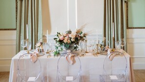 A table set for a formal event with clear chairs, a floral centerpiece, and elegant table settings. - Hotel Settles (Big Spring)