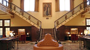 A grand lobby with a central seating area, a staircase with ornate railings, and a large painting on the wall. - Hotel Settles (Big Spring)