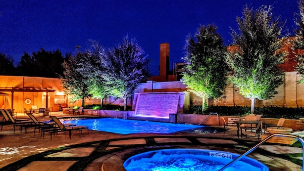 An outdoor swimming pool area with lounge chairs, a hot tub, and a waterfall feature. - Hotel Settles (Big Spring)