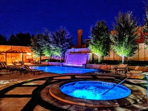 An outdoor swimming pool area with lounge chairs, a hot tub, and a waterfall feature. - Hotel Settles (Big Spring)