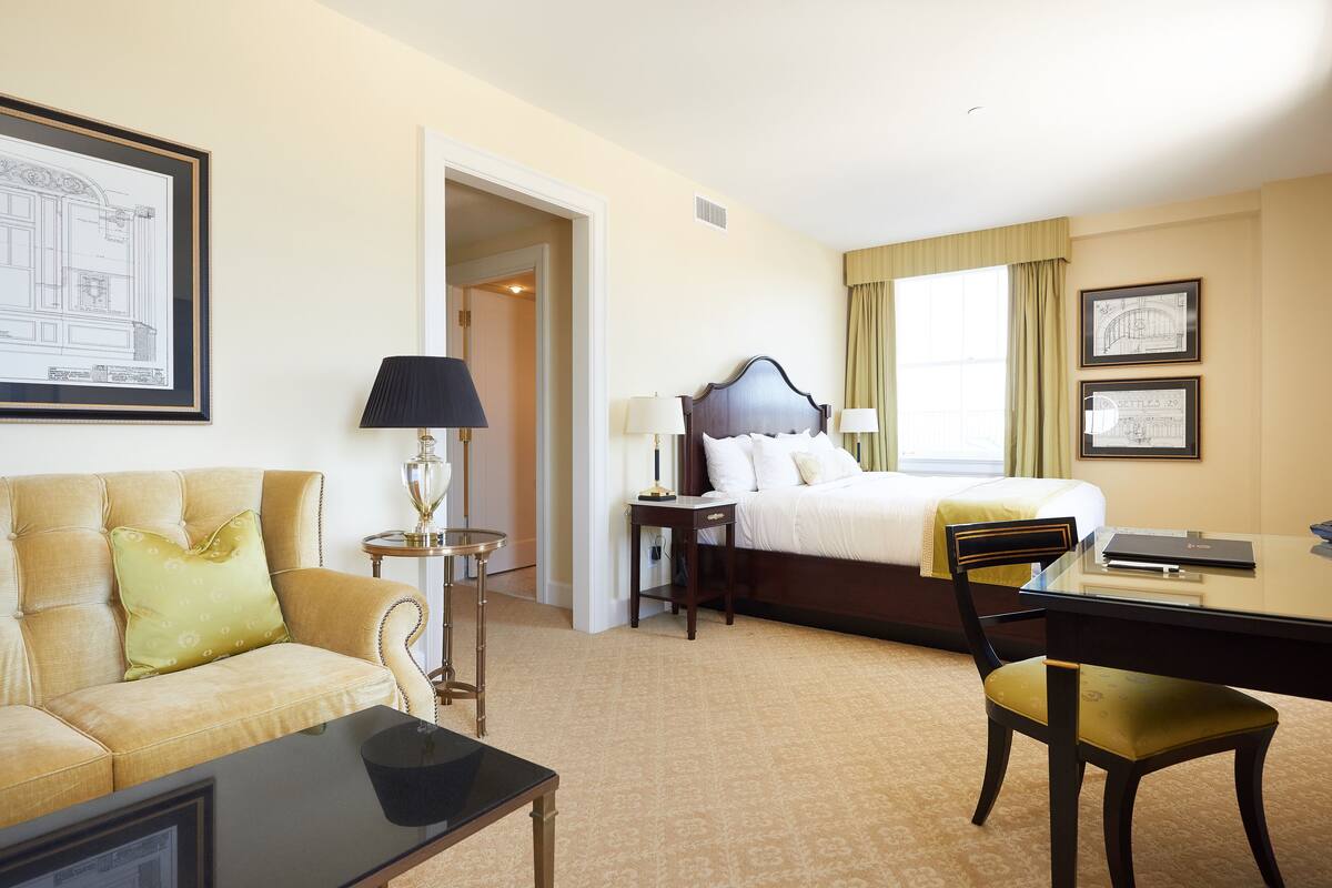 A hotel room with a bed, a desk, a chair, a lamp, and a couch.