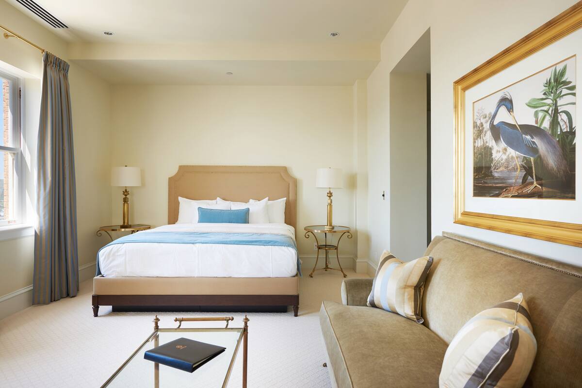 A hotel room with a large bed, two bedside tables with lamps, a sofa, and a framed picture on the wall.