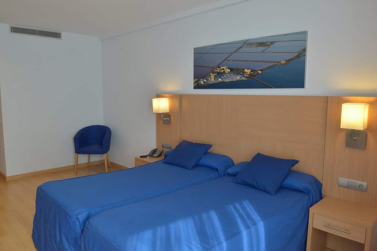 A hotel room with a large bed, two bedside tables, a chair, and a painting on the wall.