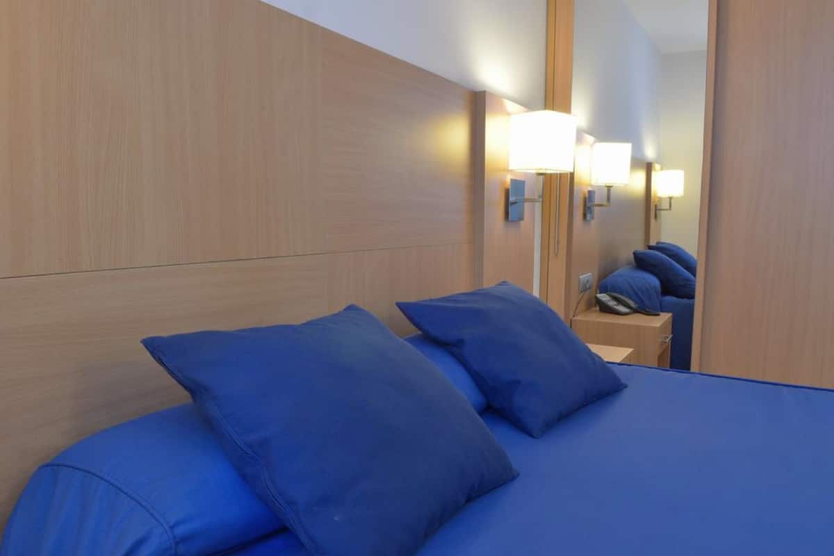 A hotel room with a wooden headboard, a bed with blue bedding, and two bedside lamps.