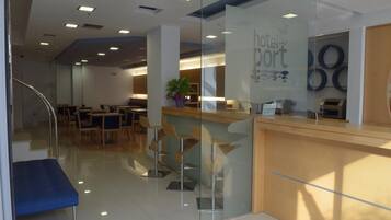 Een moderne hotel lobby met een receptiebalie, een zithoek en een trap naar een hoger niveau.