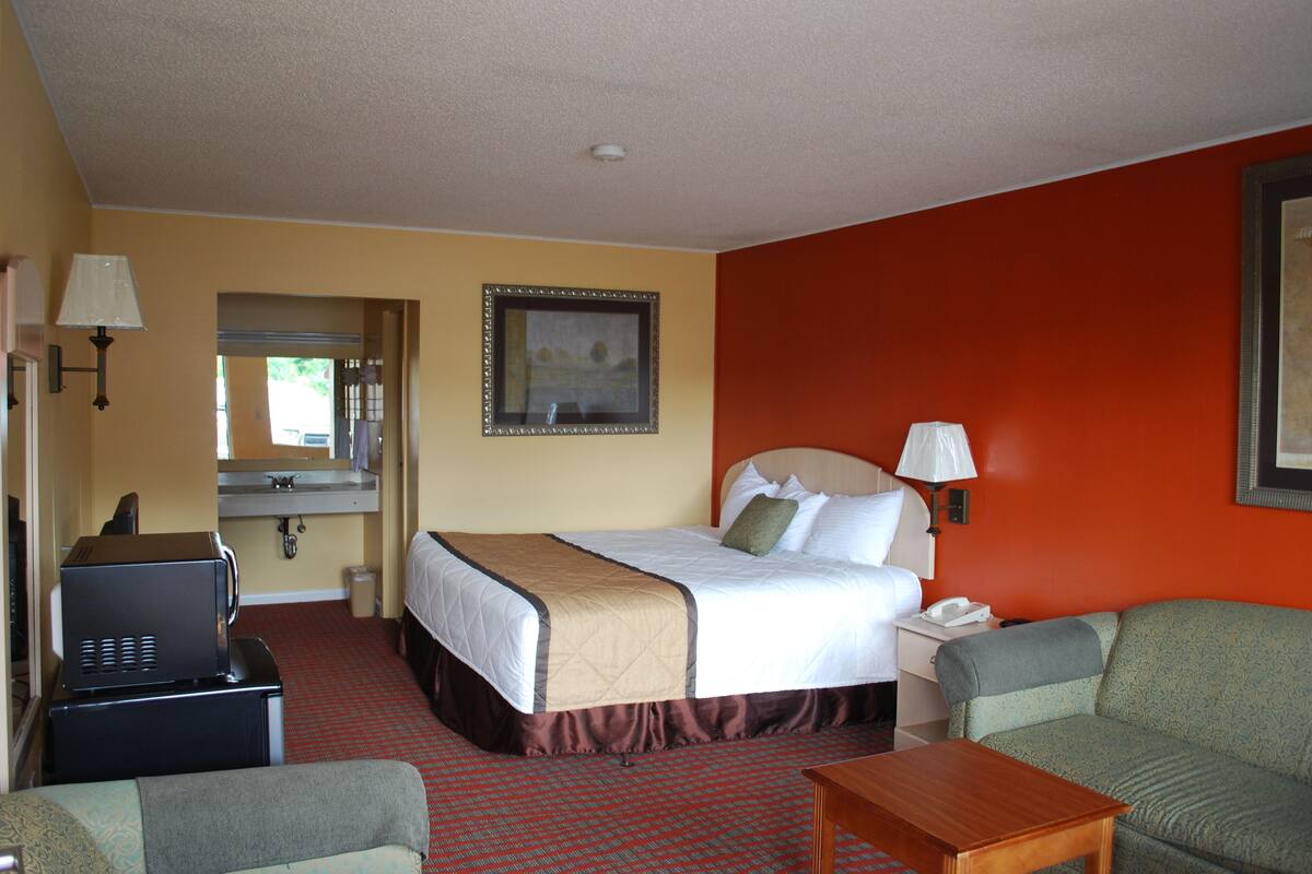 A hotel room with a bed, a desk with a telephone, a sofa, and a television.