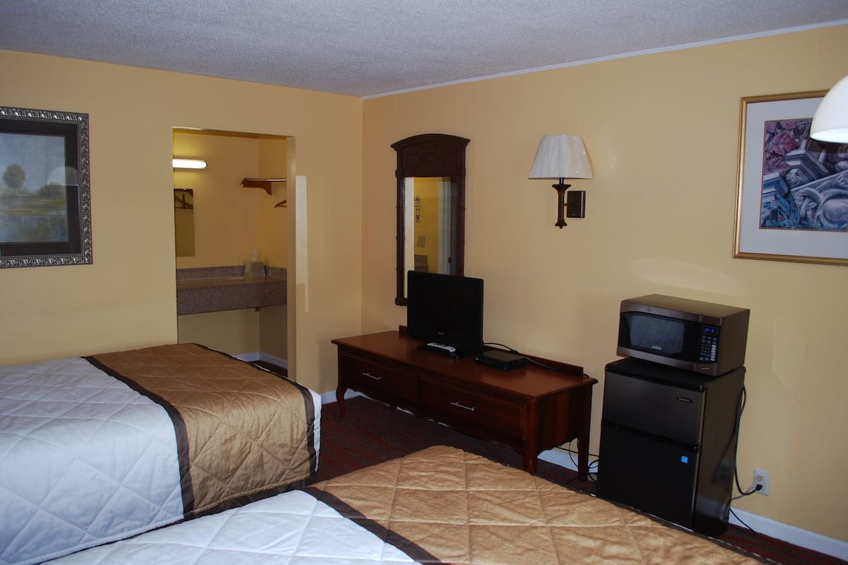 A hotel room with two beds, a television, a microwave, and a mirror.