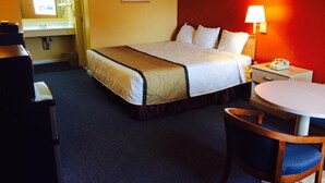 A hotel room with a bed, bedside table, lamp, chair, and a small table. - Duffy's Motel (Calhoun)