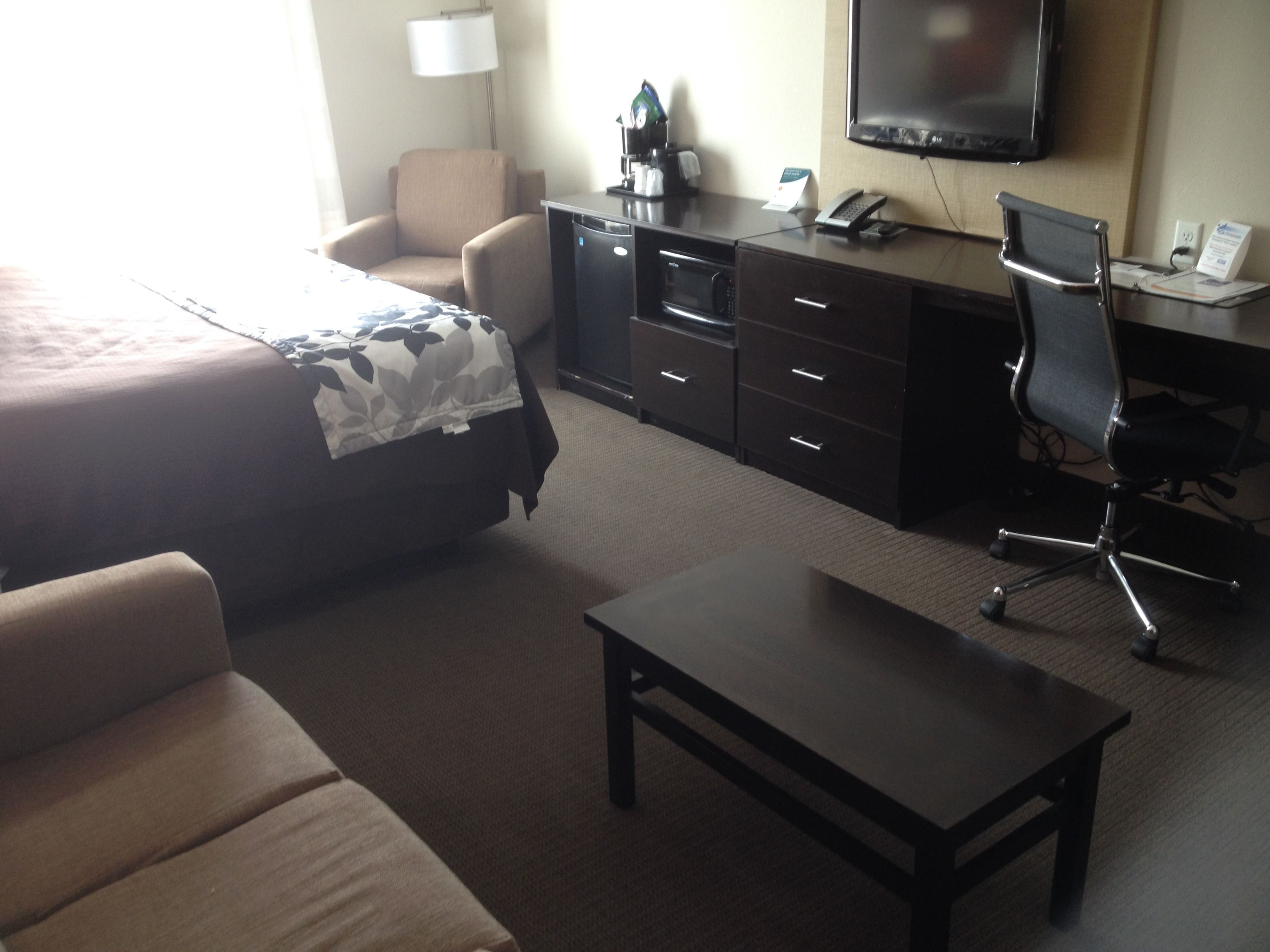 A hotel room with a bed, a desk, a chair, a coffee maker, and a television.