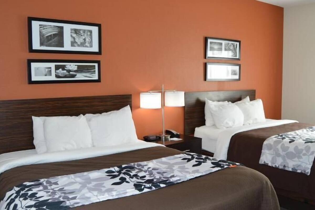 A hotel room with two beds, a nightstand with a lamp, and framed pictures on the wall.