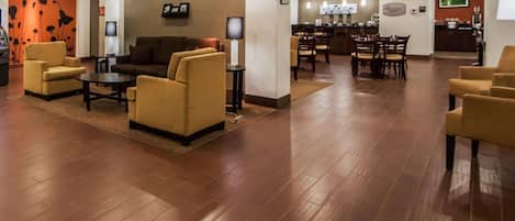 A spacious lobby with a wooden floor, comfortable seating, a reception area, and a dining setup.