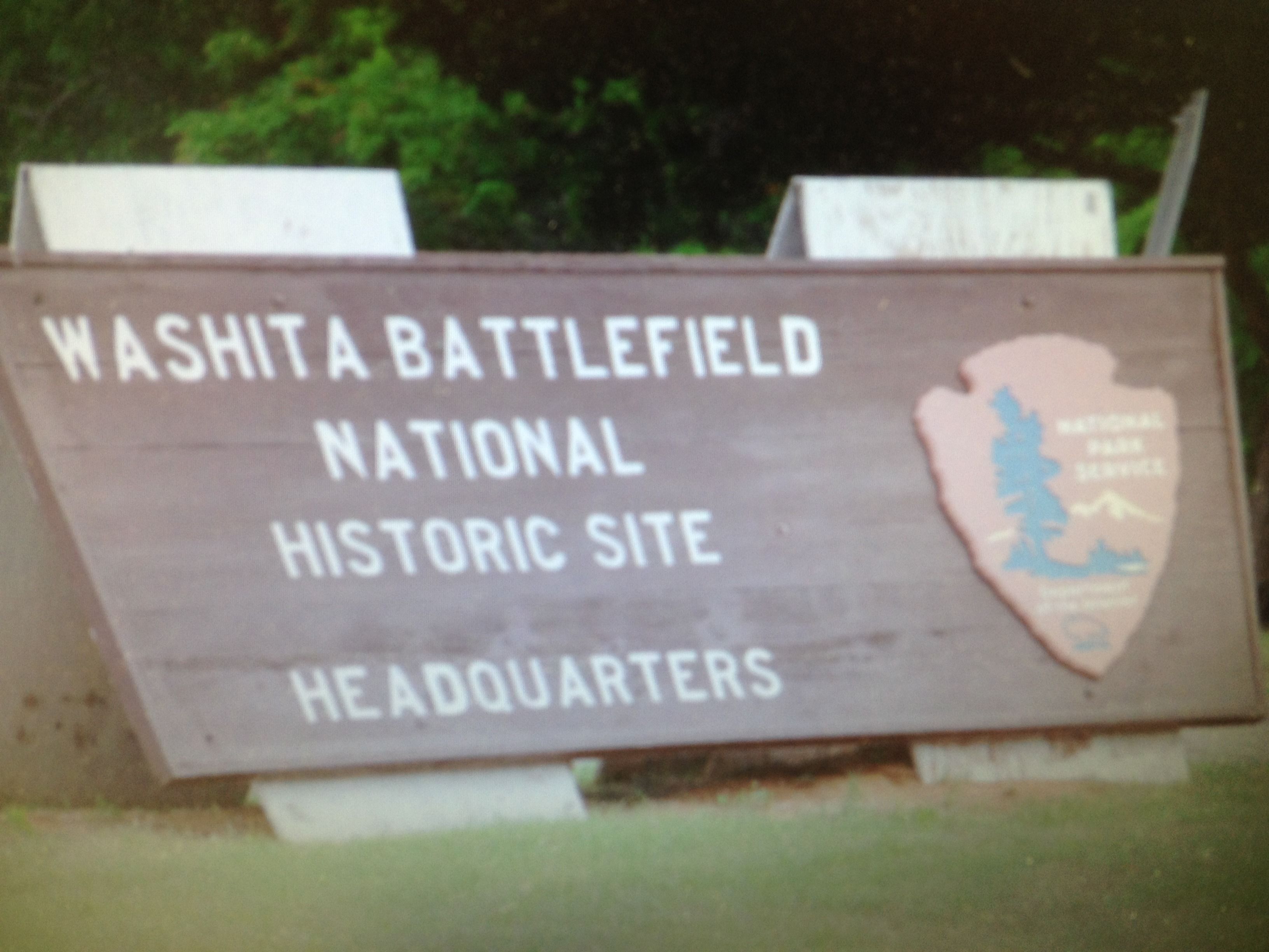 A wooden sign with text indicating it is the Washita Battlefield National Historic Site Headquarters.