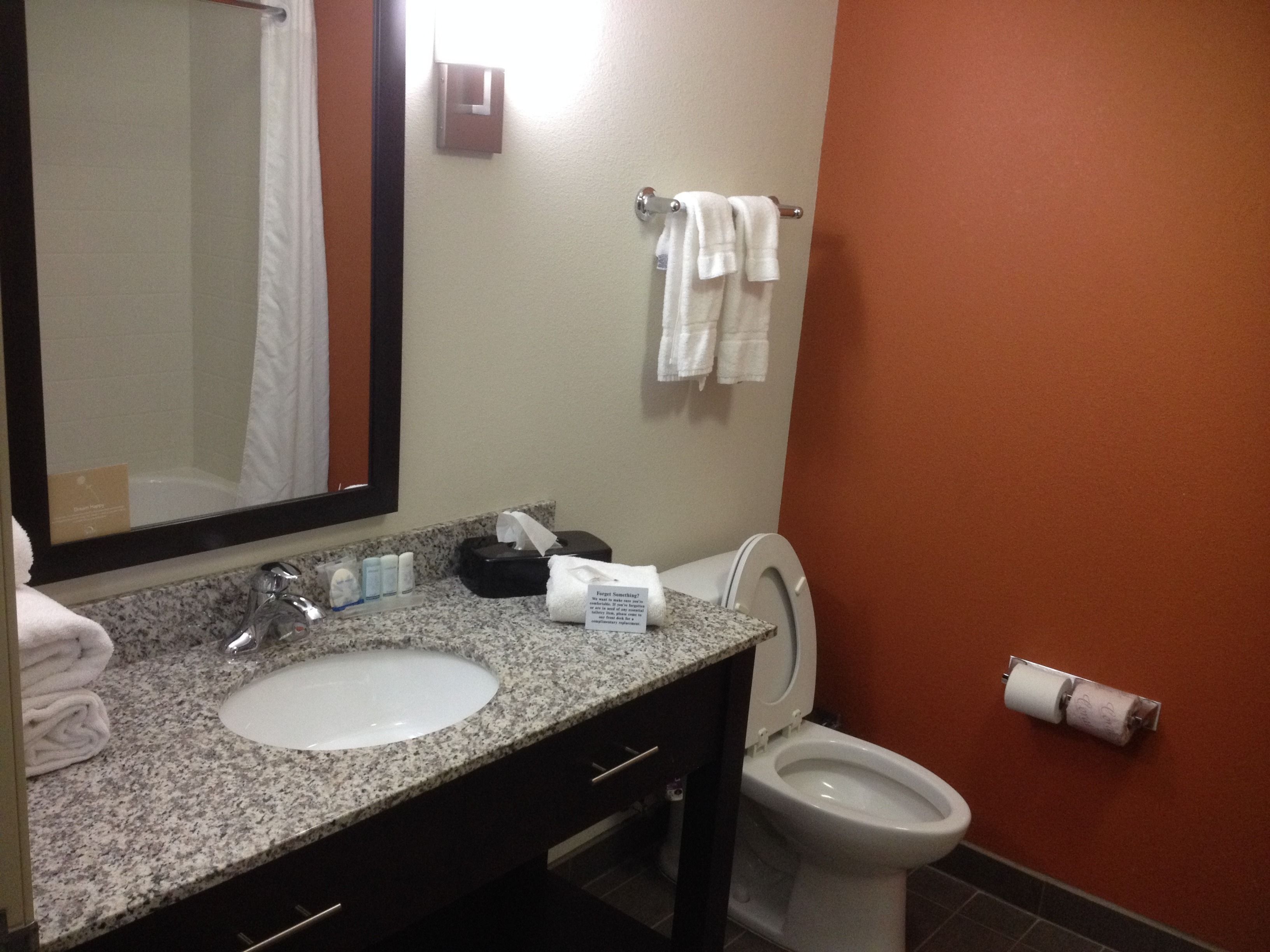 A bathroom with a granite countertop, a white sink, a mirror, a toilet, and a towel rack with towels.