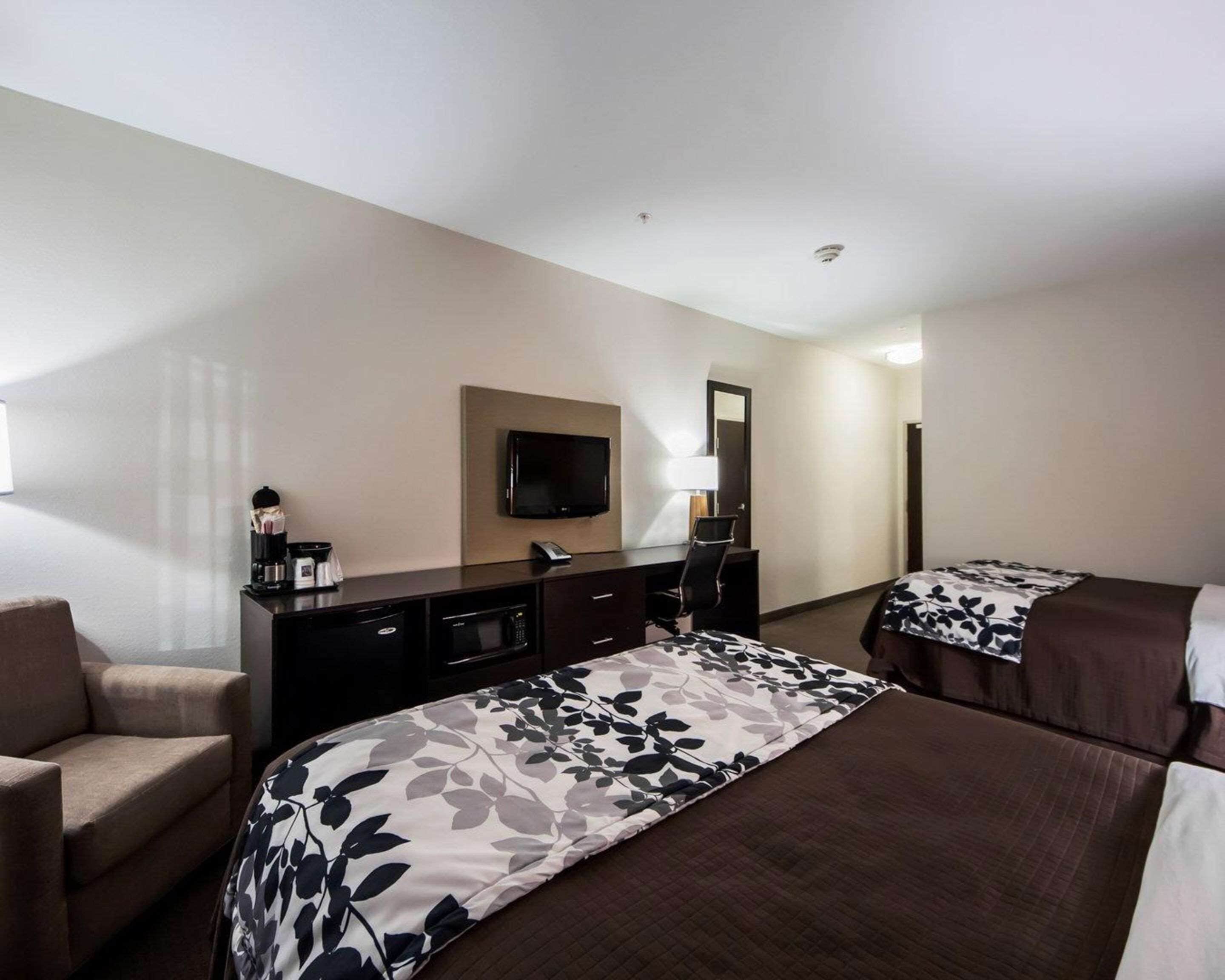 A hotel room with two beds, a desk with a flat-screen TV, a coffee maker, and a chair.