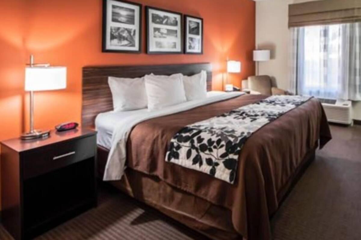 A hotel room with a large bed, a nightstand with a lamp, a chair, and a window with curtains.