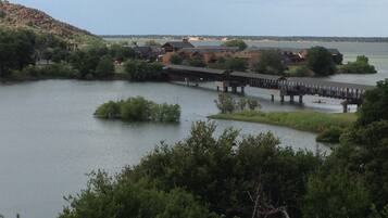 A lakeside view with a wooden bridge connecting two areas, surrounded by greenery and buildings.
