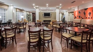 A spacious hotel dining area with multiple tables and chairs, a flat-screen TV mounted on the wall, and a fireplace. - Sleep Inn & Suites Elk City Route 66 (Elk City)