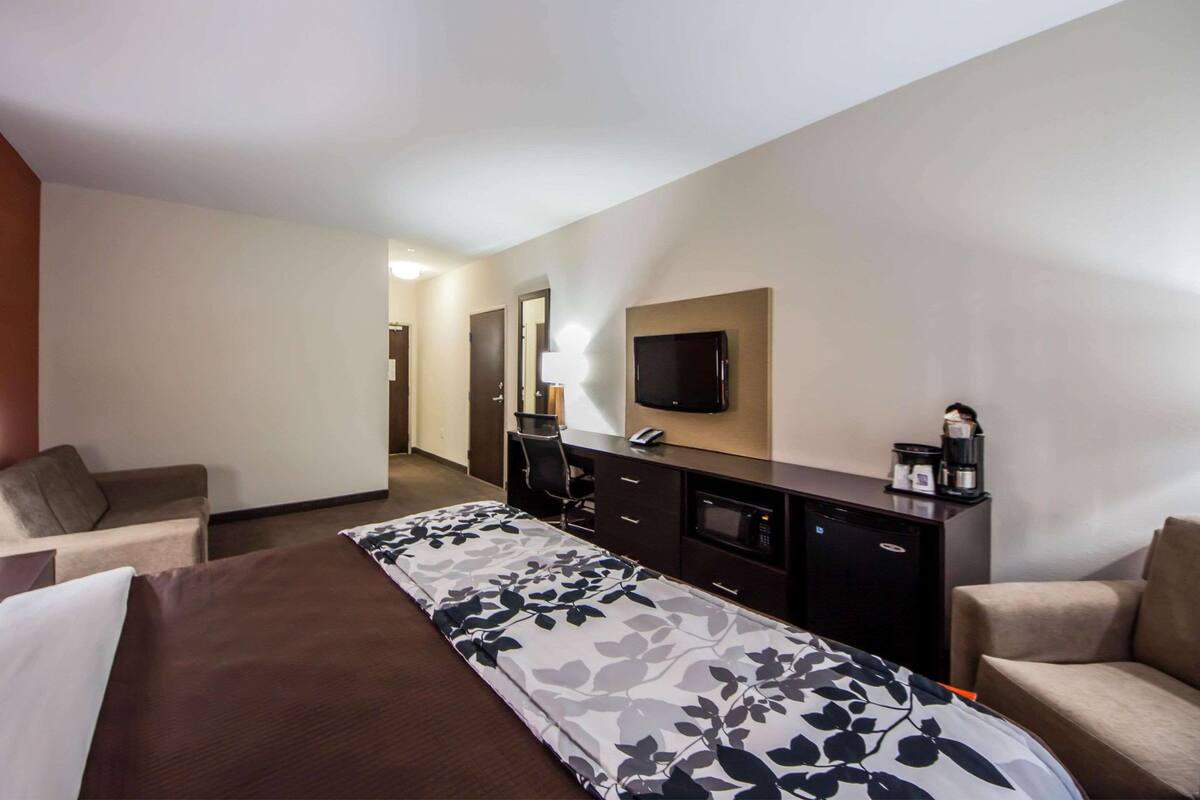 A hotel room with a large bed, a desk with a flat-screen TV, a coffee maker, and a chair.