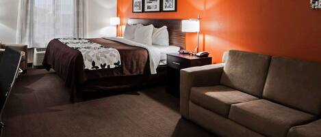 A hotel room with a bed, a desk, a chair, a sofa, and a wall with framed pictures.