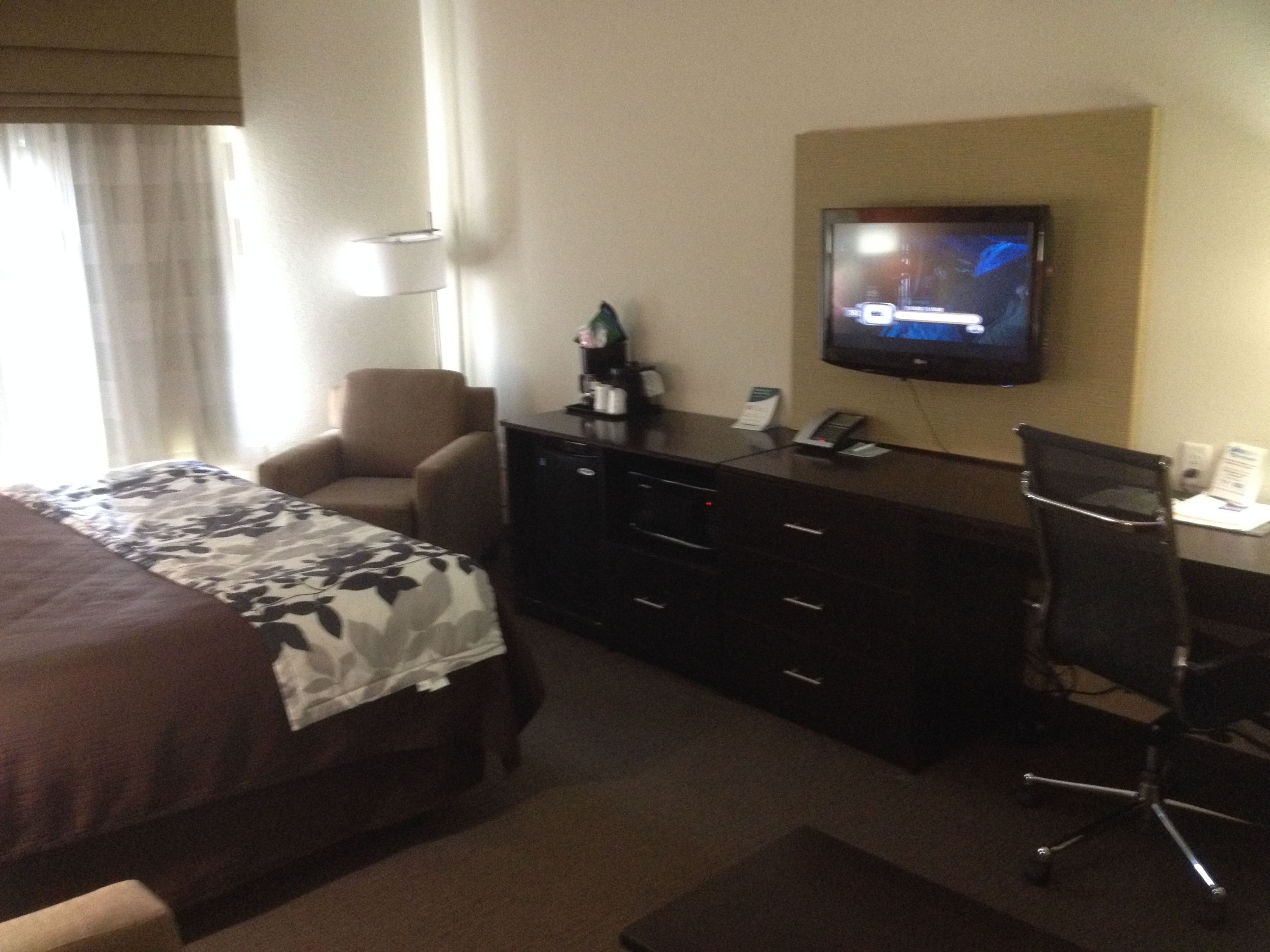 Ein Hotelzimmer mit Bett, Schreibtisch, Stuhl, Fernseher und einem Fenster mit Vorhängen.