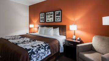A hotel room with a large bed, two bedside tables with lamps, a chair, and three framed pictures on the wall.