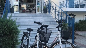 Un edificio con una escalera que lleva a un balcón, dos bicicletas estacionadas en la entrada y plantas en macetas.