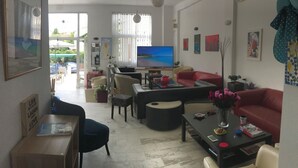 A living room with a TV, sofas, a coffee table, and a dining area with chairs. - Victor-Eleni Hotel (Kassandra)