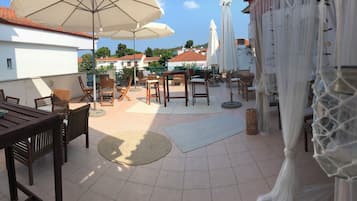 An outdoor patio with wooden furniture, white umbrellas, and a view of buildings in the background.