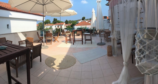An outdoor patio with wooden furniture, white umbrellas, and a view of buildings in the background.