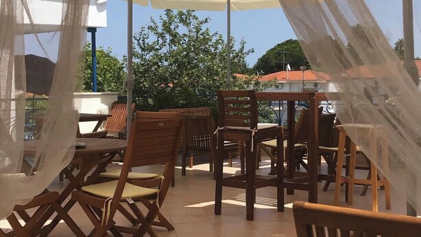 An outdoor patio with wooden furniture and beige umbrellas. - Victor-Eleni Hotel (Kassandra)