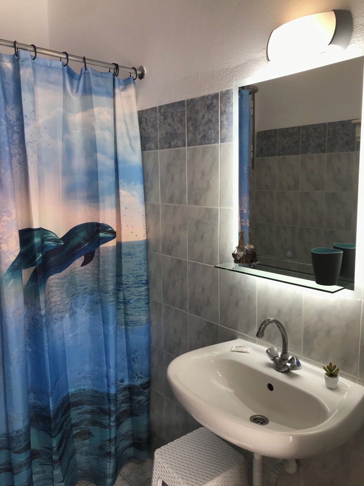 Un bagno con tenda da doccia raffigurante delfini, un lavandino e uno specchio sopra.