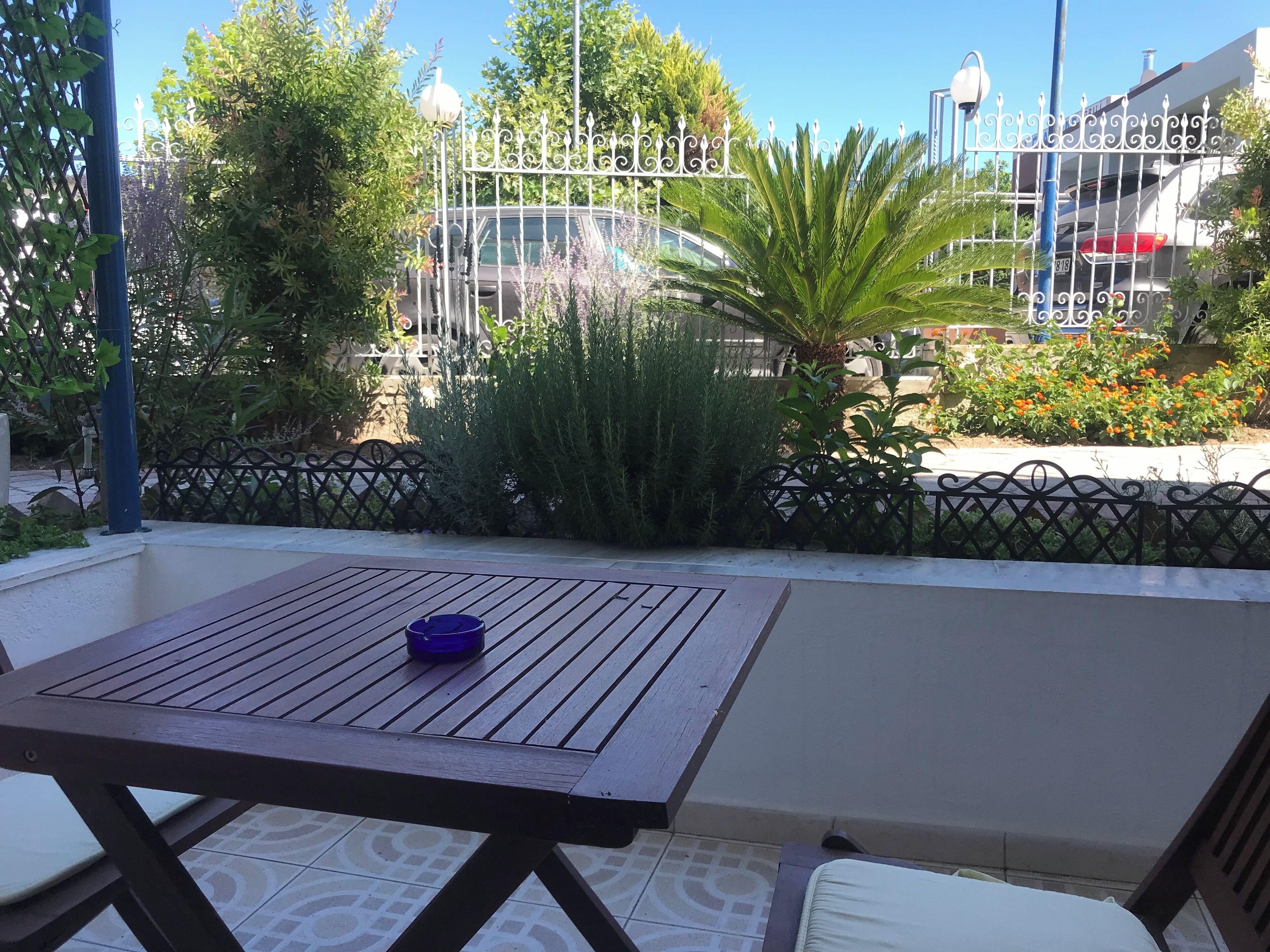 A patio with a table and chairs, surrounded by a metal fence and various plants.