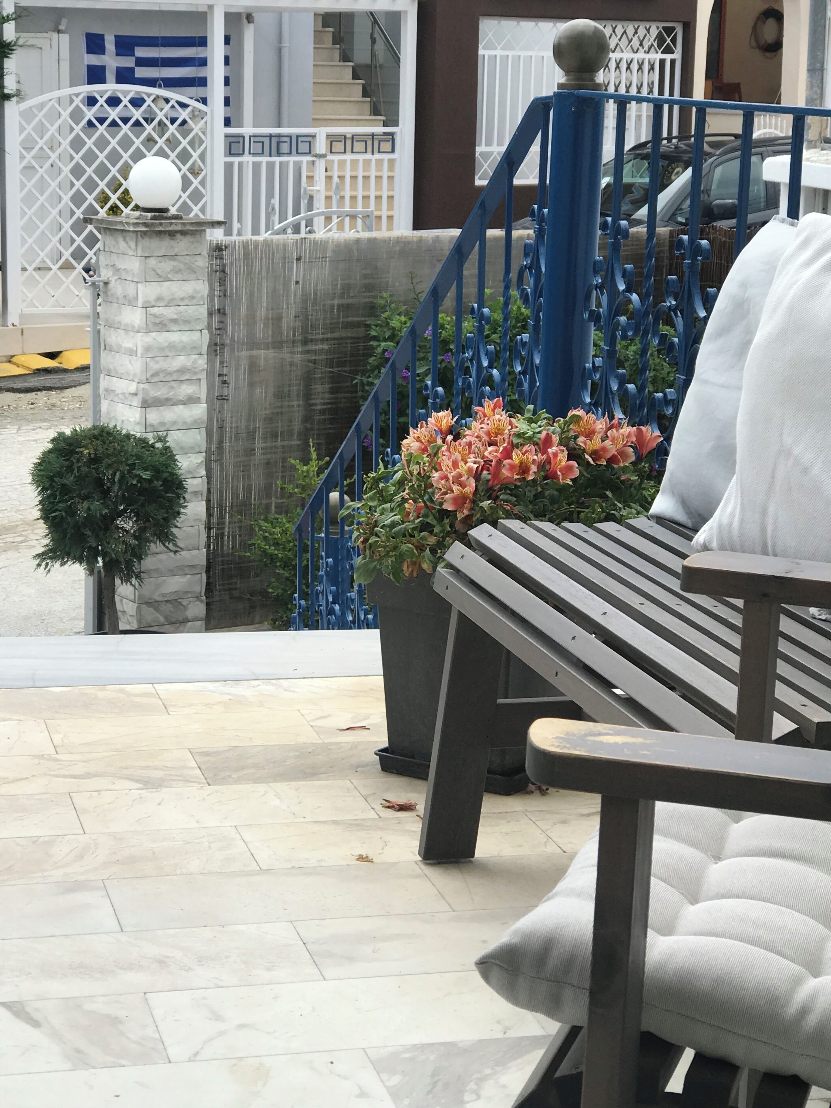 Un banco con un macetero lleno de flores, una escalera con barandillas azules y un edificio blanco al fondo.