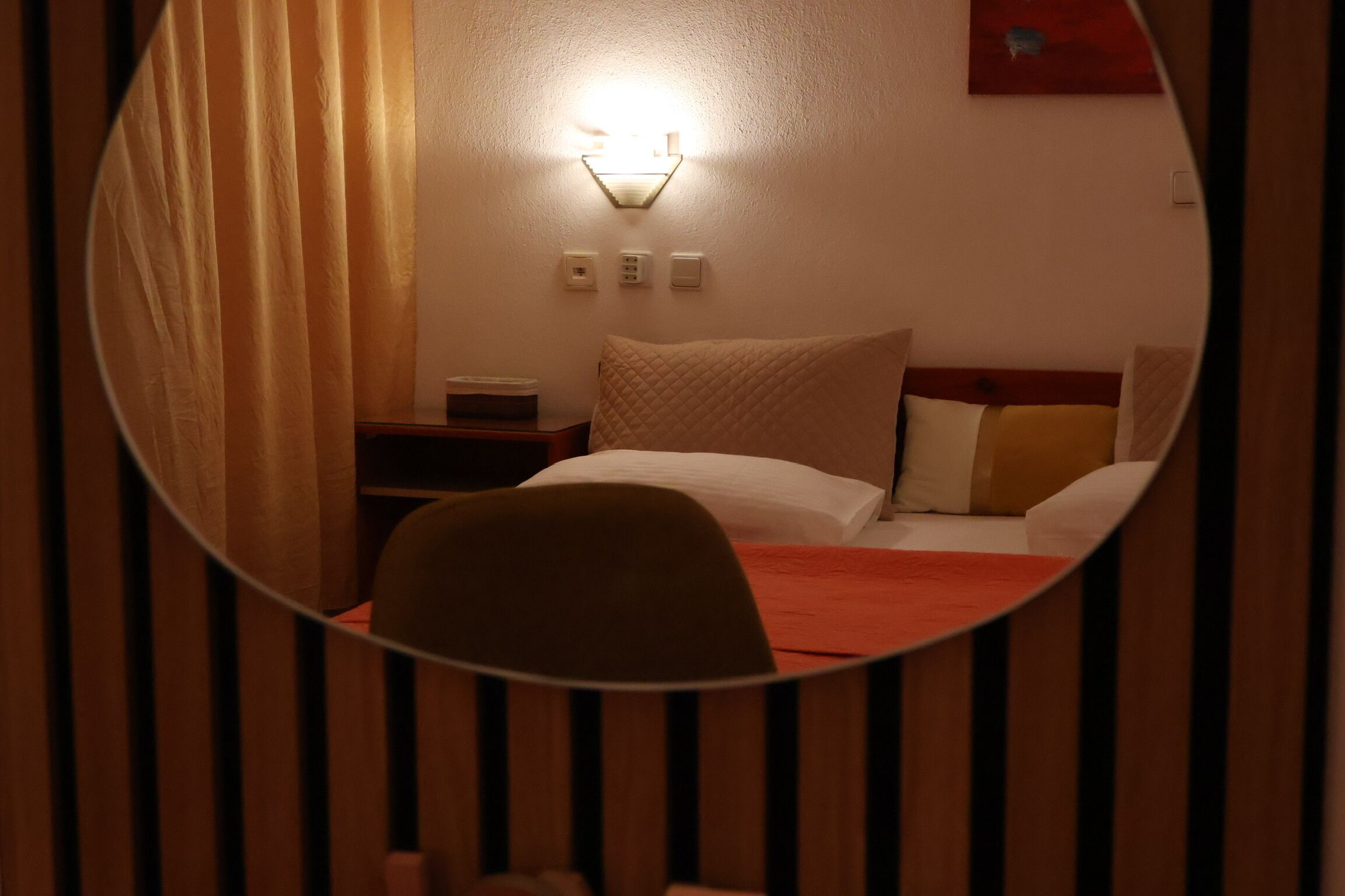 Een hotelkamer met een bed, nachtkastje, lamp en spiegel.