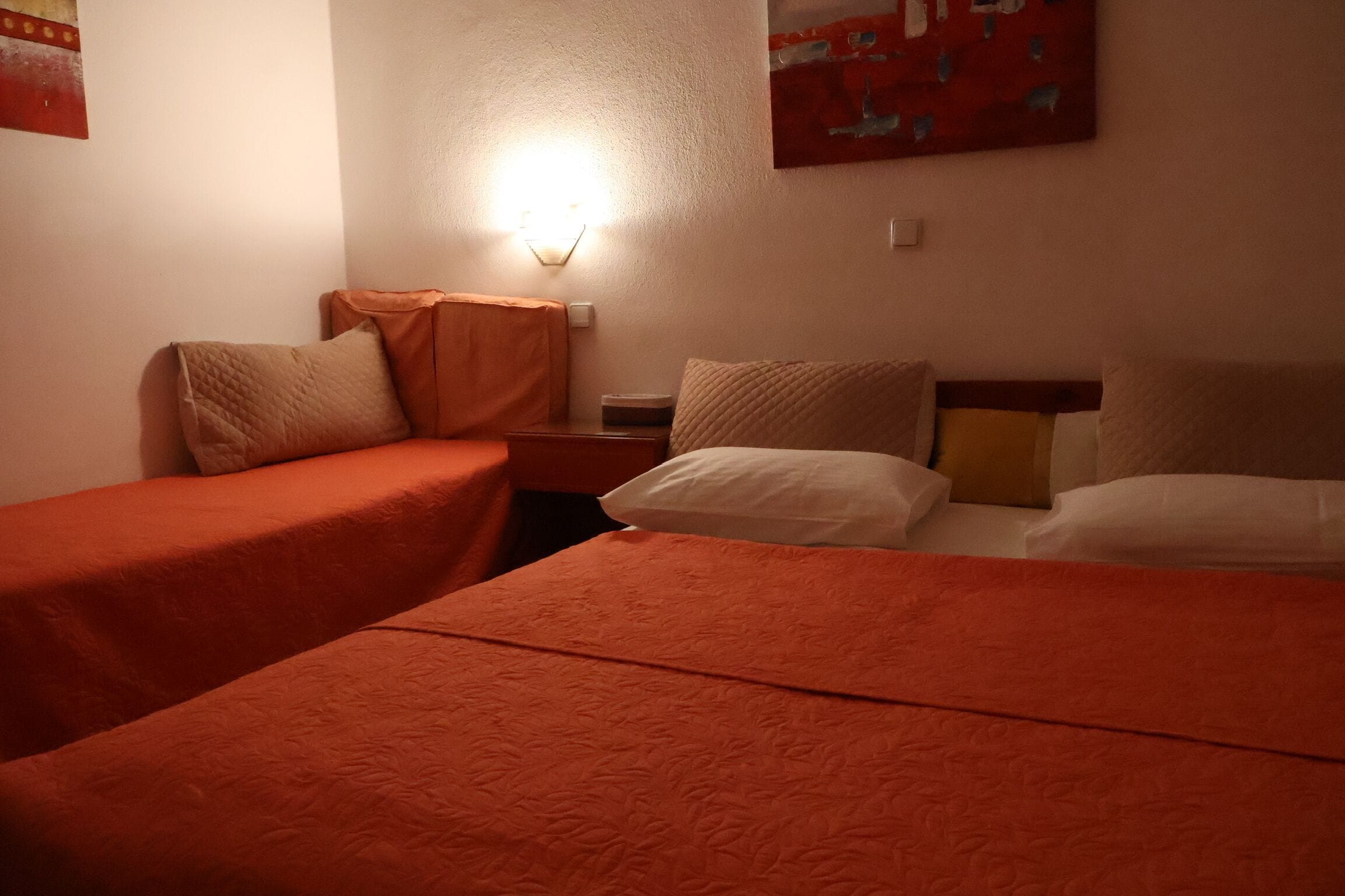 A hotel room with two beds, a nightstand, and a wall-mounted light.
