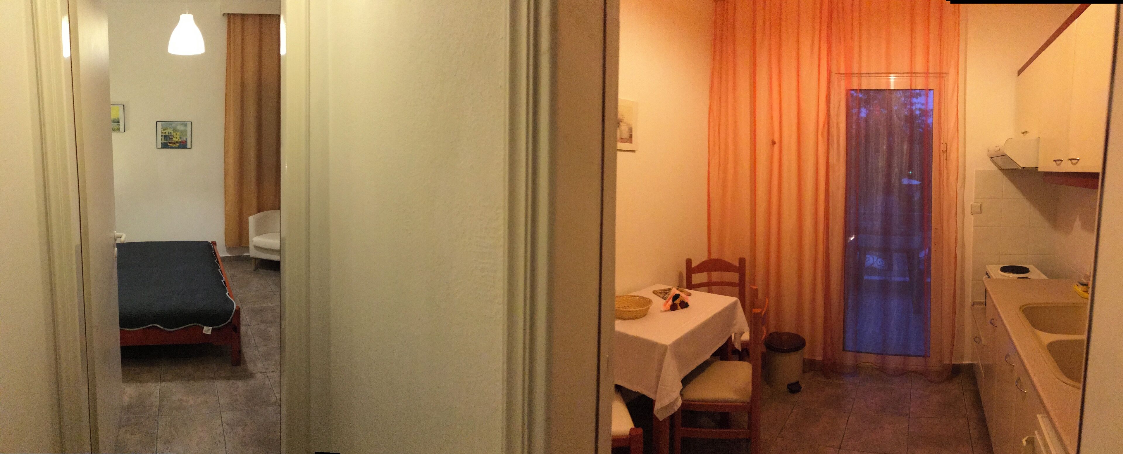 A narrow hallway leading to a small dining area with a table and chairs, a single bed, and a bathroom with a sink and mirror.