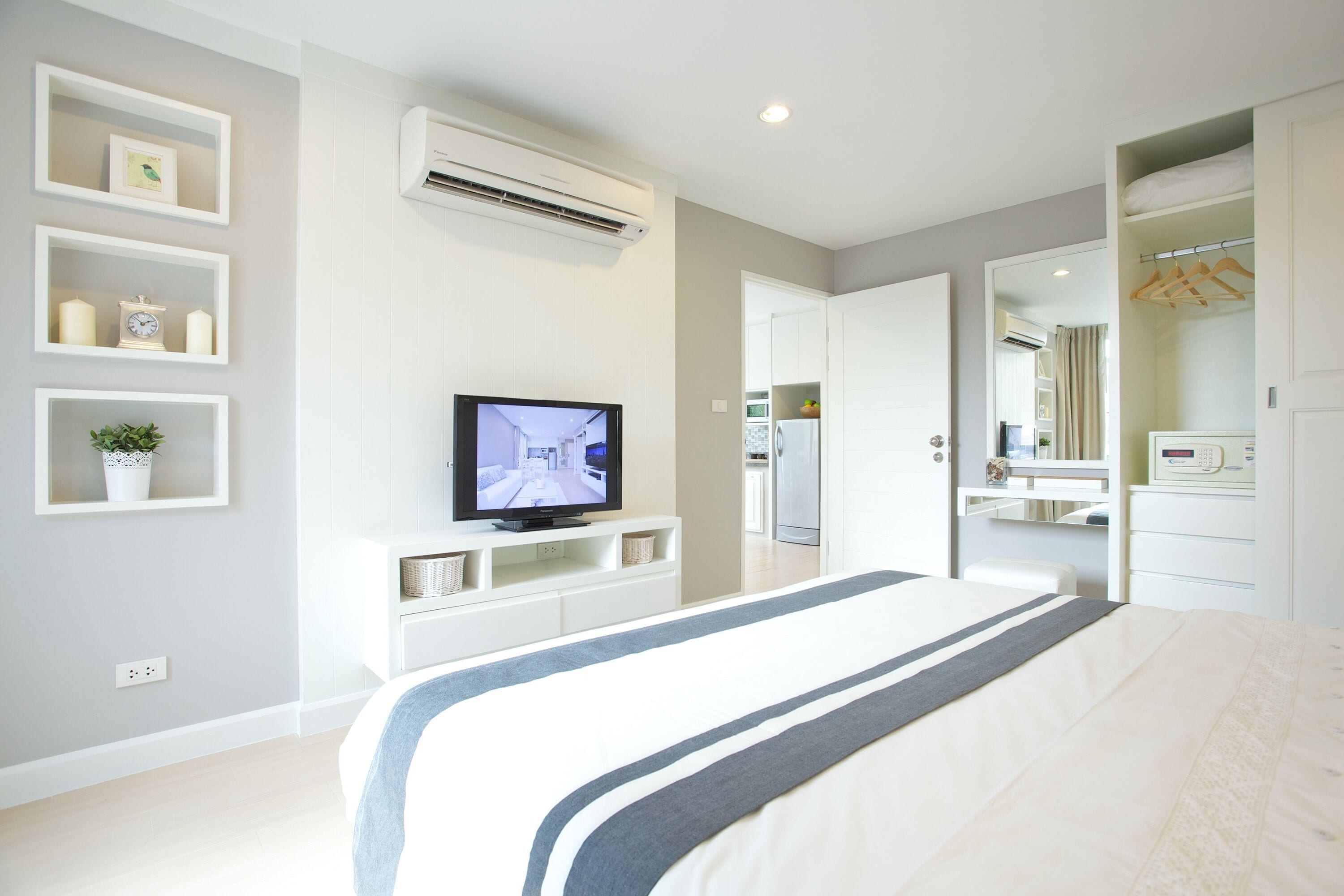 A modern bedroom with a large bed, a TV on a white console, a wardrobe, and a mirror.