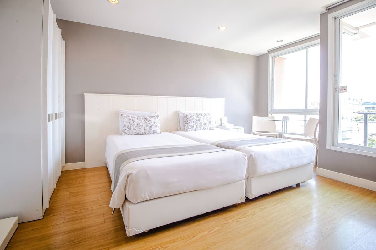 Une chambre moderne avec deux lits, une grande fenêtre et une vue sur la ville.
