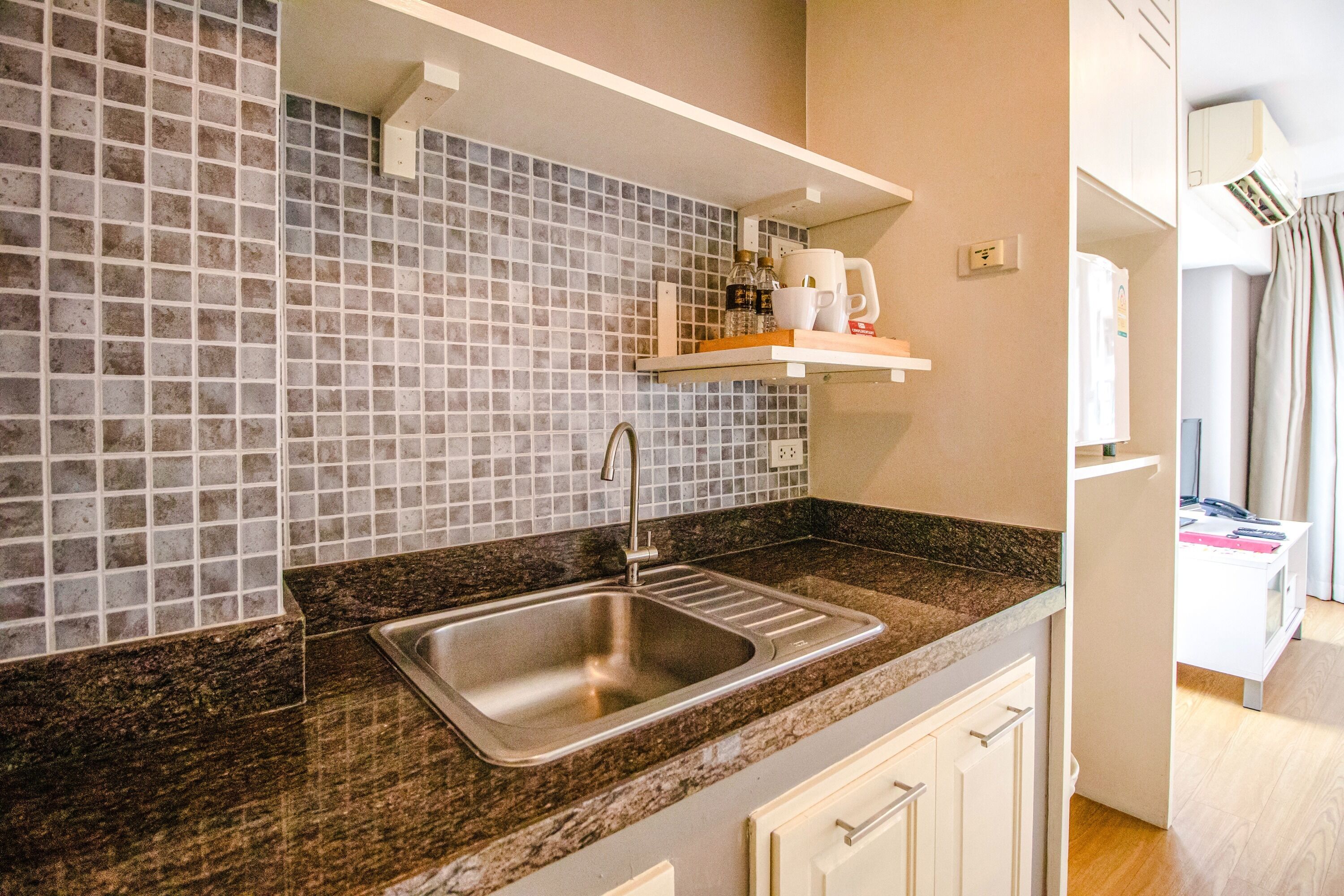 A kitchen with a stainless steel sink, a tiled backsplash, and a wooden countertop.